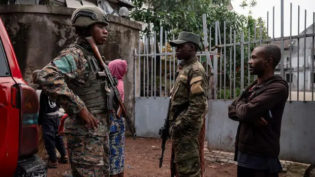 Deux militaires armés accompagnés d'un civil en arrière-plan en discussion dans une zone urbaine